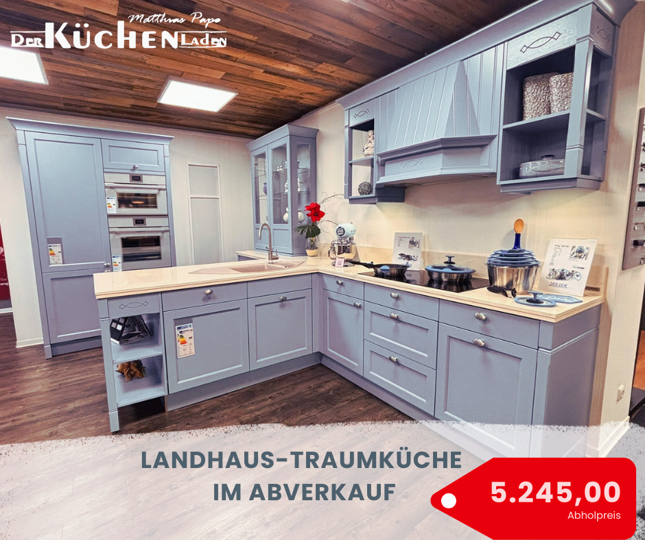 **ALT-Text:** Landhausstil-Traumküche in sanftem Blau mit hochwertigen Einbaugeräten und großzügiger Arbeitsfläche. Stilvolle Fronten mit klassischen Details, offene Regale und elegante Glaselemente verleihen der Küche eine einladende Atmosphäre. Jetzt im Abverkauf für 5.245,00 € als Abholpreis erhältlich.